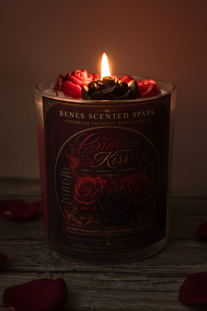Crimson Kiss coconut wax candle glowing in a dark romantic setting with crimson and black rose wax toppers and scattered red rose petals.