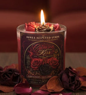 Crimson Kiss coconut wax candle burning in a warm romantic setting, surrounded by deep burgundy roses, rose petals, and autumn leaves.