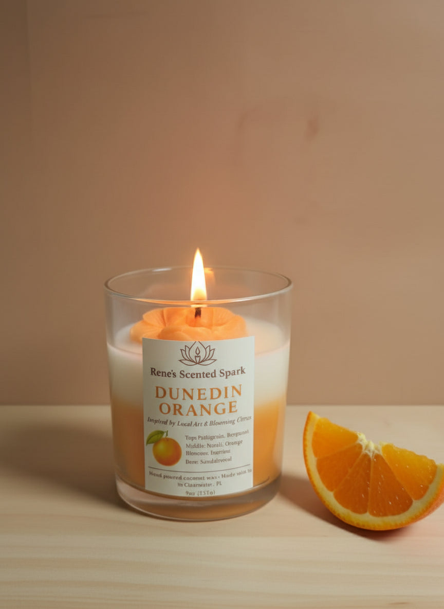 Candle labeled 'Dunedin Orange' with a slice of orange on a wooden surface.