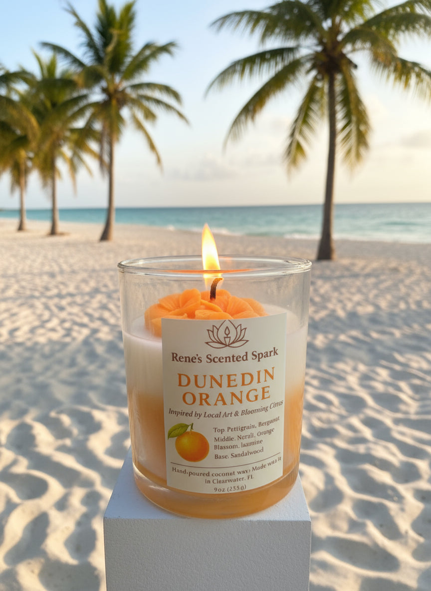 Candle labeled 'Dunedin Orange' on a beach with palm trees and ocean in the background