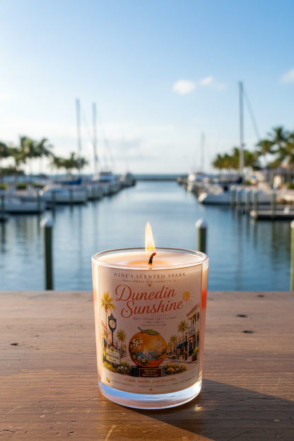 Candle labeled 'Dunedin Sunshine' on a wooden surface with boats in the background 