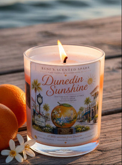Candle labeled 'Dunedin Sunshine' with a scenic label design on a wooden surface.