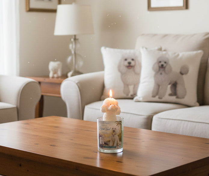 Hand-poured coconut wax poodle candle with a white poodle-shaped wax topper and Elegant Soul label displayed on a wooden coffee table in a cozy living room with decorative poodle pillows in the background.