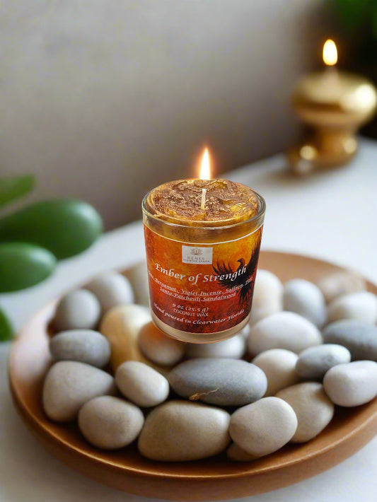 Spiritual candle collection displayed on a wooden table with Ember of Strength candle topped with phoenix and dragon, and Tranquil Spirit candle beside a Buddha figure. Surrounded by crystals, stones, and greenery — symbolic gift candles for meditation, healing, and renewal