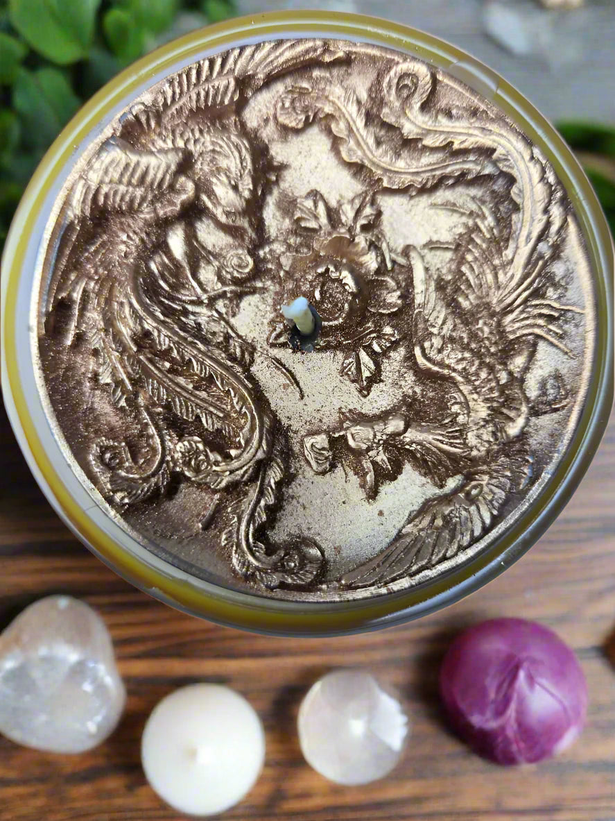 Spiritual candle collection displayed on a wooden table with Ember of Strength candle topped with phoenix and dragon, and Tranquil Spirit candle beside a Buddha figure. Surrounded by crystals, stones, and greenery — symbolic gift candles for meditation, healing, and renewal