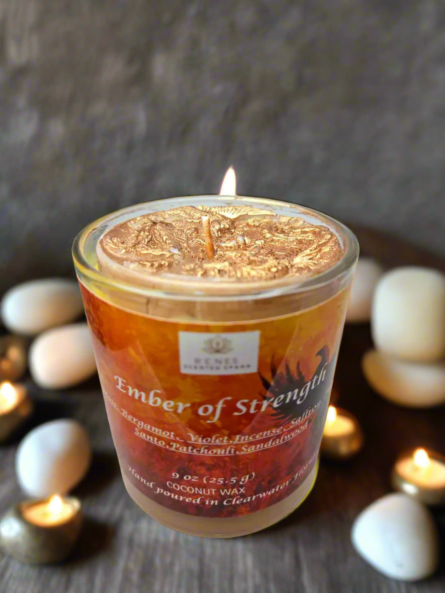 Spiritual candle collection displayed on a wooden table with Ember of Strength candle topped with phoenix and dragon, and Tranquil Spirit candle beside a Buddha figure. Surrounded by crystals, stones, and greenery — symbolic gift candles for meditation, healing, and renewal