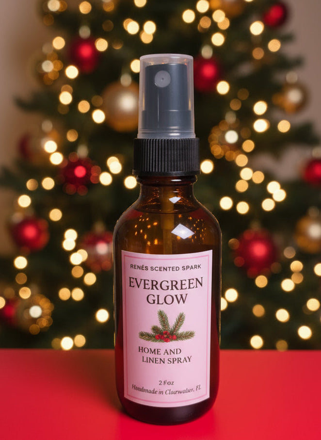Amber glass bottle labeled “Evergreen Glow Home & Linen Spray” by René’s Scented Spark, displayed in front of a glowing Christmas tree with red and gold ornaments.