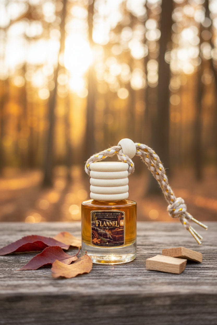Flannel car freshener by Rene's Scented Spark displayed on rustic wood with autumn leaves, wood pieces, and a softly blurred forest in warm golden sunlight.
