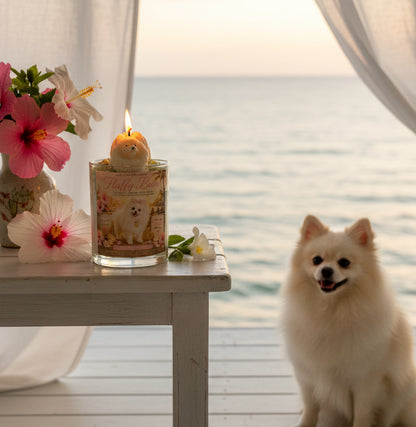 A luxury lit  candle featuring a handcrafted Pomeranian dog wax topper displayed on a white coastal porch overlooking the ocean. 
