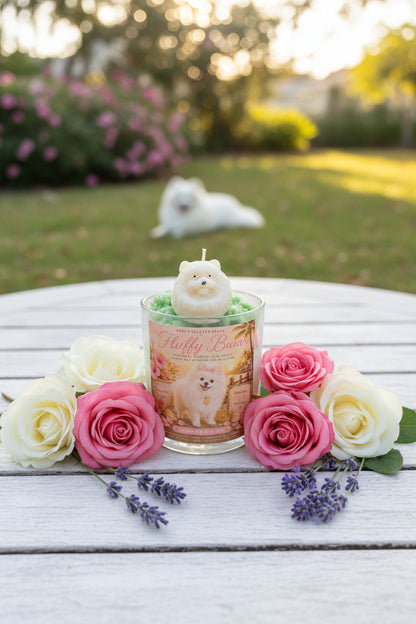 A luxury candle with a realistic white pomeranian dog wax topper displayed on a white garden table surrounded by blooming roses and lavender.