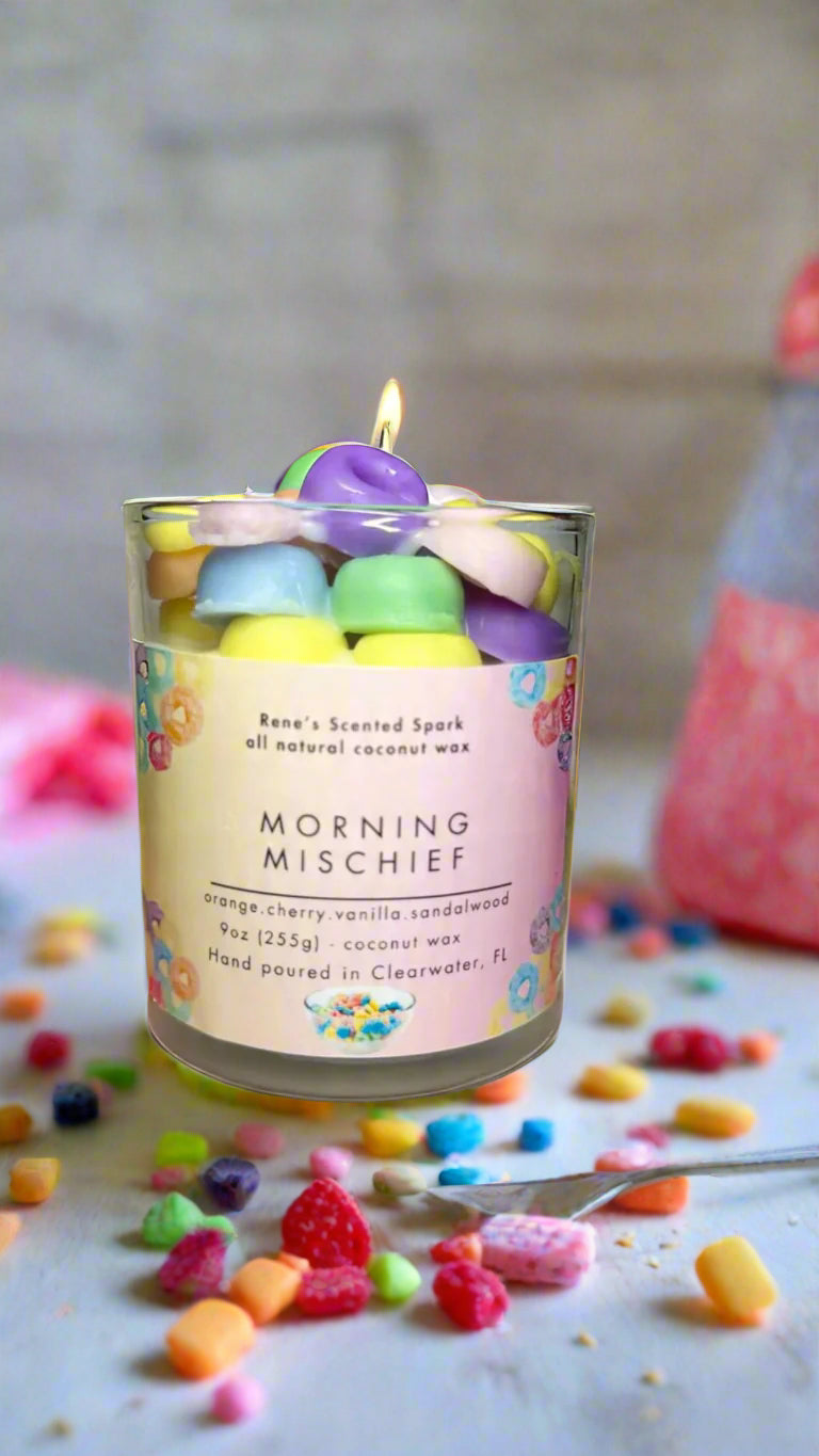 Morning Mischief fruity cereal candle glowing beside a colorful cereal bowl, spoon, and milk