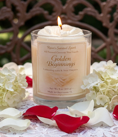 Candle labeled 'Golden Beginnings' with flowers and petals on a lace tablecloth