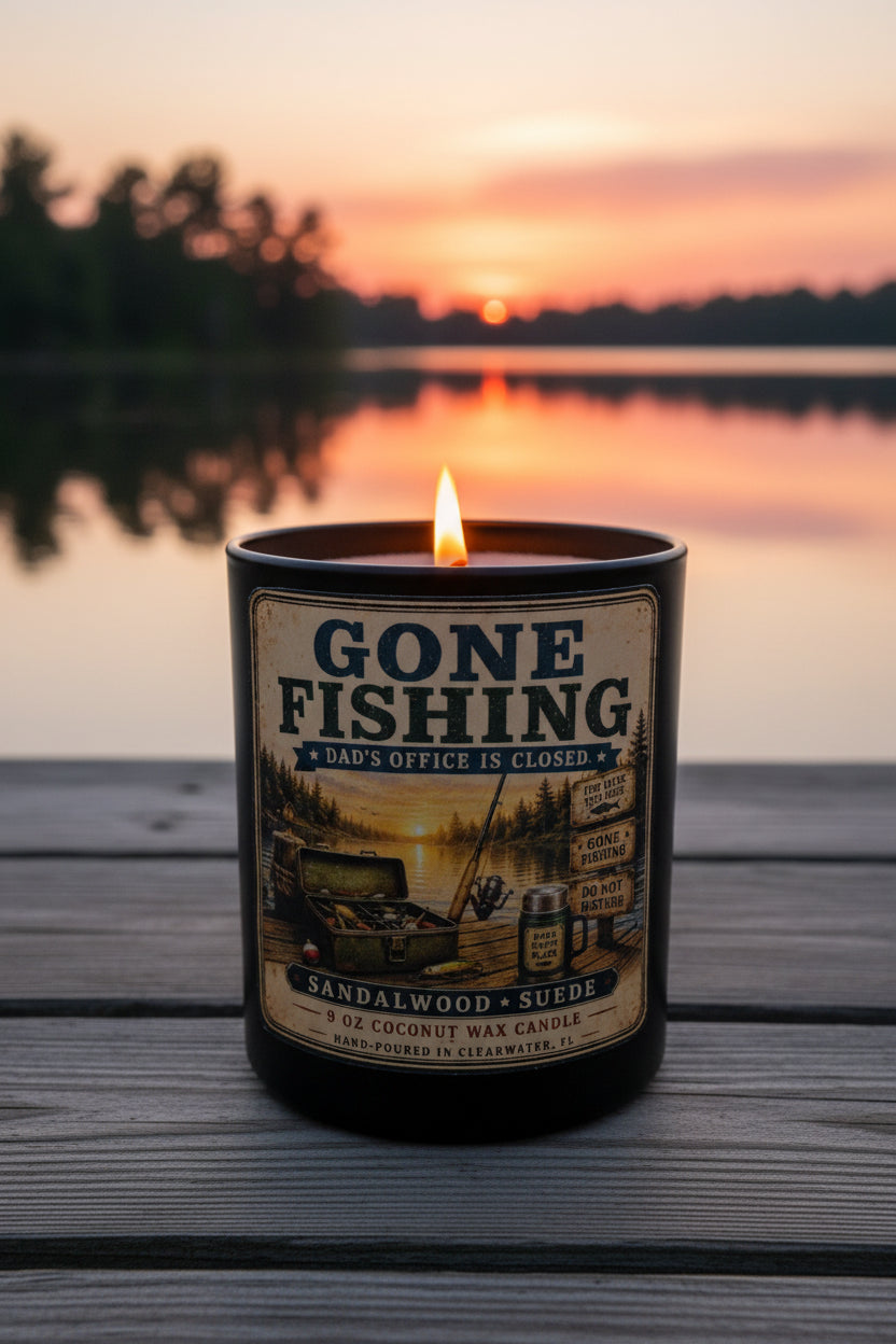 Gone Fishing candle glowing warmly on a wooden dock at sunset with beautiful orange and pink water reflection