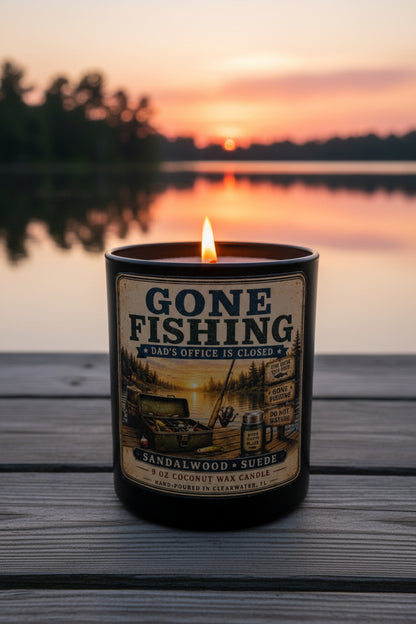 Gone Fishing candle glowing warmly on a wooden dock at sunset with beautiful orange and pink water reflection