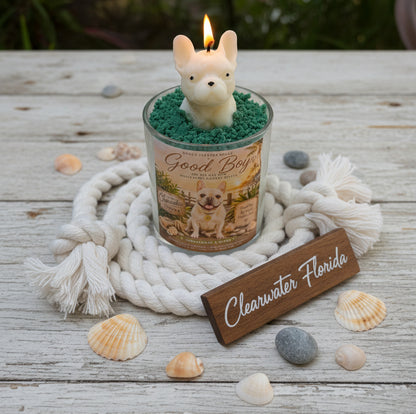 Candle with a dog-shaped wick holder on a wooden surface with shells and a 'Clearwater Florida' sign.