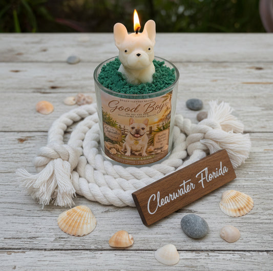 Candle with a dog-shaped wick holder on a wooden surface with shells and a 'Clearwater Florida' sign.