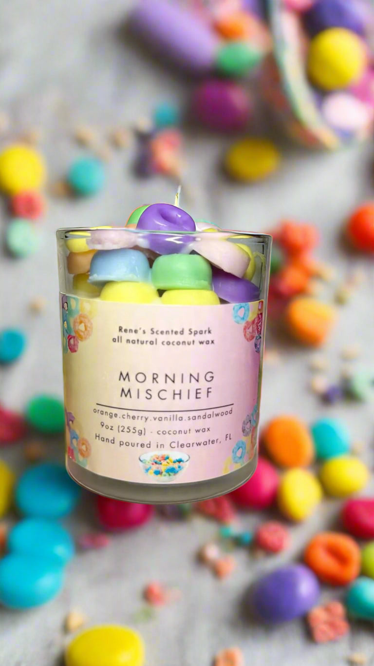 Morning Mischief fruity cereal candle glowing beside a colorful cereal bowl, spoon, and milk