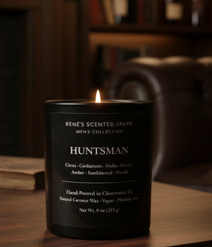 Lit black glass Huntsman candle from Rene’s Scented Spark on a wooden table with leather chair and bookshelf in a warm, cozy setting