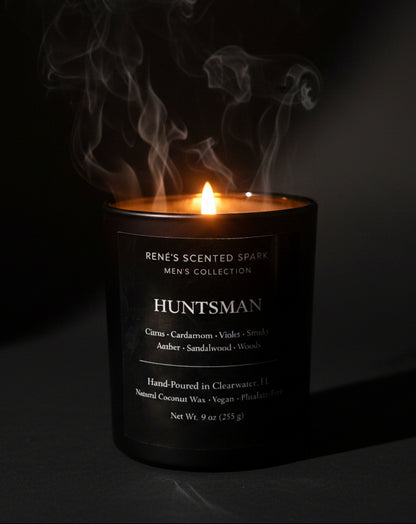 Black “Huntsman” candle by Rene’s Scented Spark glowing on mossy log in a misty forest with warm sunlight