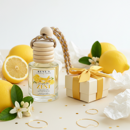 Simply the Zest lemon cake and vanilla car freshener by Rene’s Scented Spark displayed with fresh lemons, citrus blossoms, and a cream gift box with yellow ribbon. 🍋🎁