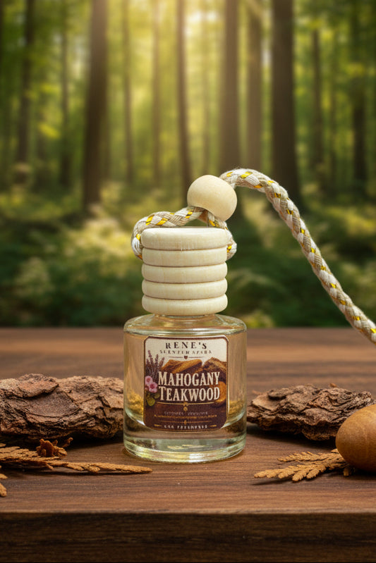 Mahogany Teakwood hanging car freshener with wooden diffuser cap displayed on natural wood with tree bark and oak accents against a softly sunlit forest background.