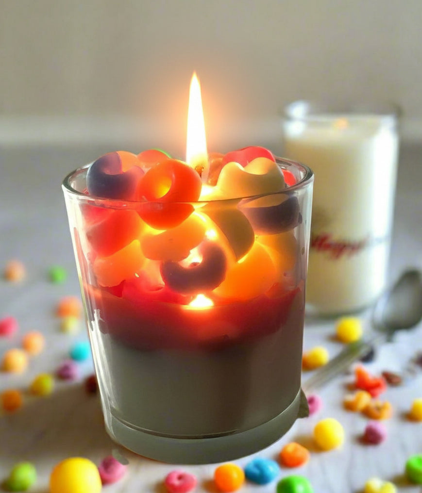 Morning Mischief coconut wax candle with colorful cereal-inspired wax pieces next to a bowl of fruit loops, evoking cheerful Saturday mornings.