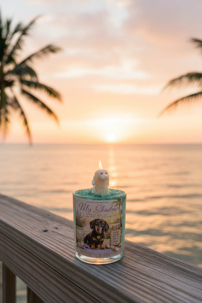 Candle with a dog design on a wooden ledge by the ocean at sunset