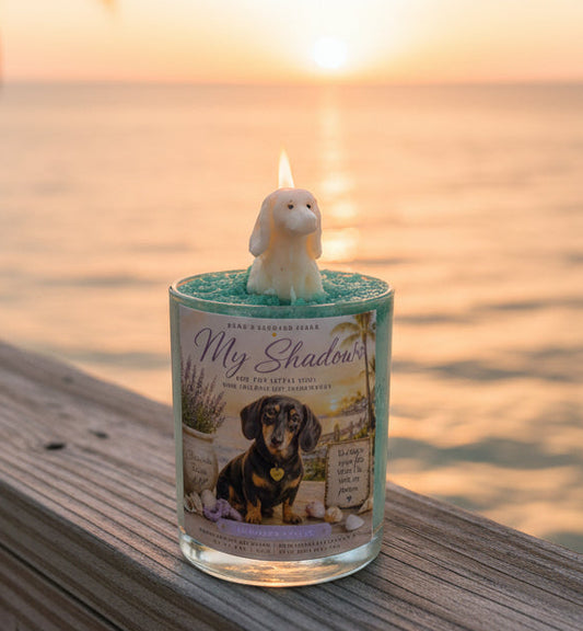 Candle with a dog design on a wooden ledge by the ocean at sunset