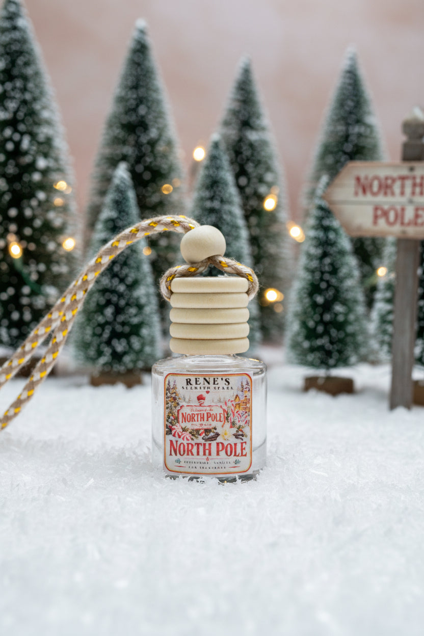 North Pole peppermint and vanilla car freshener by Rene’s Scented Spark displayed in a snowy Christmas scene with frosted pine trees, warm lights, and a North Pole sign.