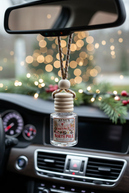North Pole peppermint and vanilla hanging car freshener by Rene’s Scented Spark displayed from a car rearview mirror with festive Christmas lights and evergreen décor