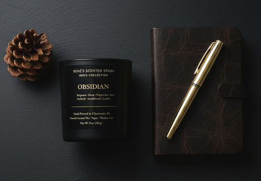 Obsidian-scented candle, leather notebook, and gold pen on a dark surface