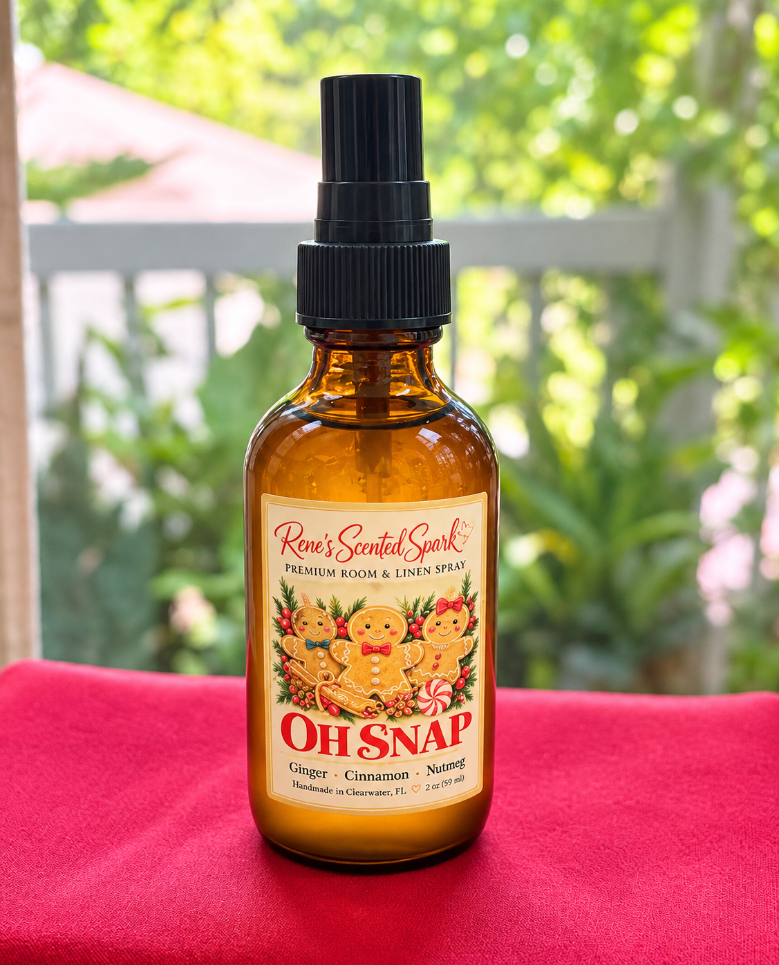 Rene's Scented Spark Oh Snap 2 oz gingerbread room spray in amber glass bottle with gingerbread man label on red fabric outdoors