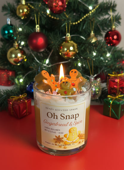 Candle labeled 'Oh Snap Gingerbread & Spice' with gingerbread men on top, in front of a decorated Christmas tree.