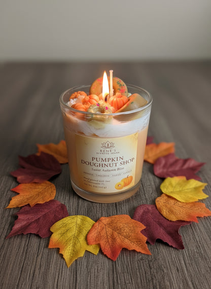 Candle with pumpkin doughnut design surrounded by fall leaves on a wooden surface