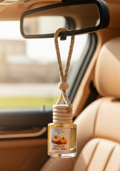 Pumpkin Donut Shop hanging car freshener by Renes Scented Spark displayed from a rearview mirror inside a car with a warm tan interior.