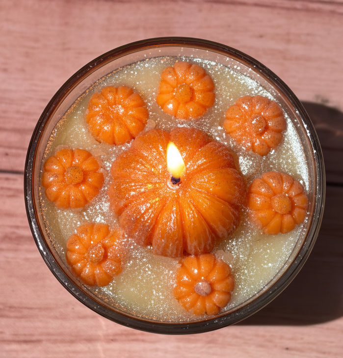 Top view of lit Apple Orchard Bliss coconut wax candle by Rene's Scented Spark featuring a handcrafted pumpkin wax topper surrounded by miniature pumpkins and shimmering coconut wax.