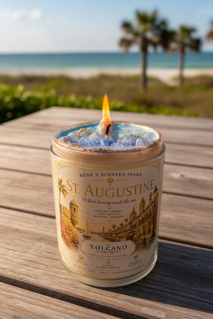 Lit St. Augustine coconut wax candle by Rene's Scented Spark displayed on a wooden table overlooking a Florida beach, featuring a vintage-inspired city label and handcrafted blue wax.