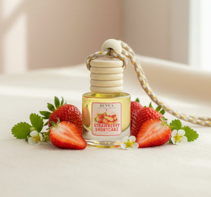 Strawberry Shortcake car freshener with wooden diffuser cap surrounded by fresh whole and sliced strawberries and delicate white blossoms in a bright, softly lit setting.