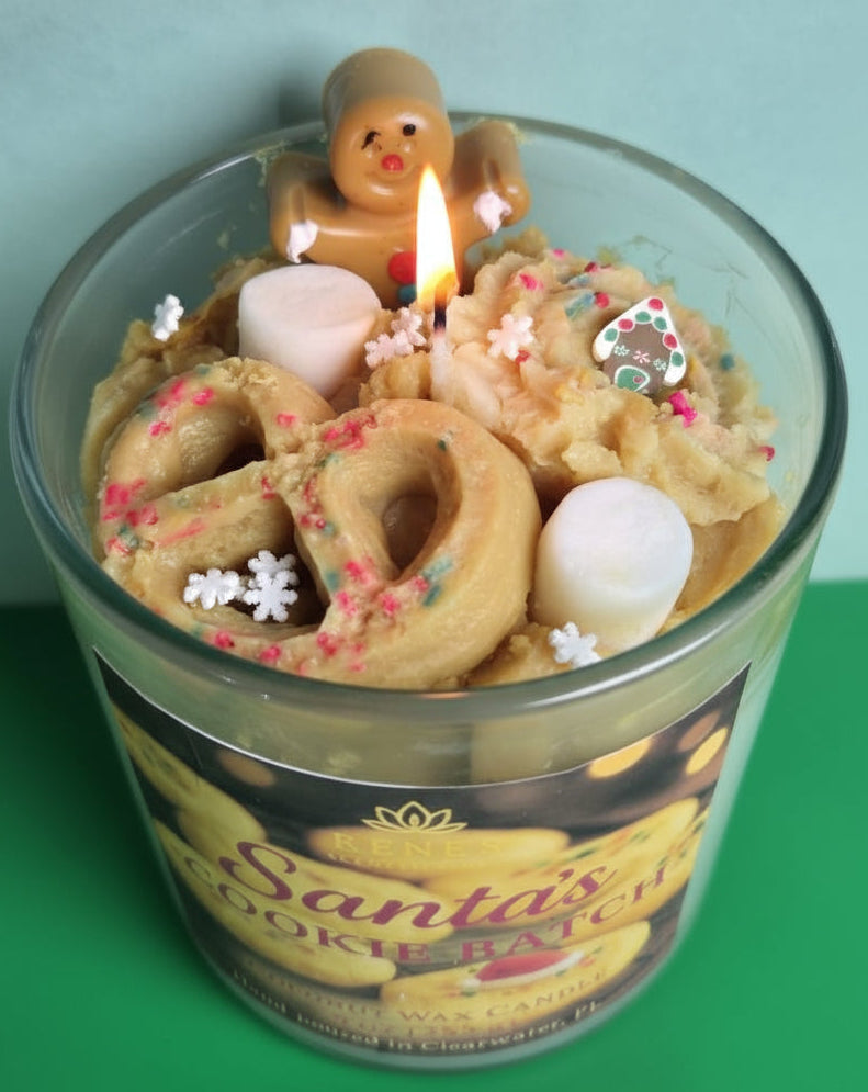 Candle in a glass jar labeled 'Santa's Cookie Batch with gingerbread man and cookie decorations.