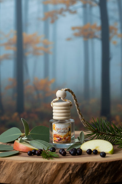 Sweater Weather car freshener by Rene’s Scented Spark displayed with apple slices, sage, eucalyptus, pine, and juniper berries against a misty autumn forest background