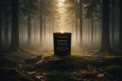 Lit black glass Huntsman candle from Rene’s Scented Spark placed on a moss-covered log in a foggy forest with soft golden light filtering through trees