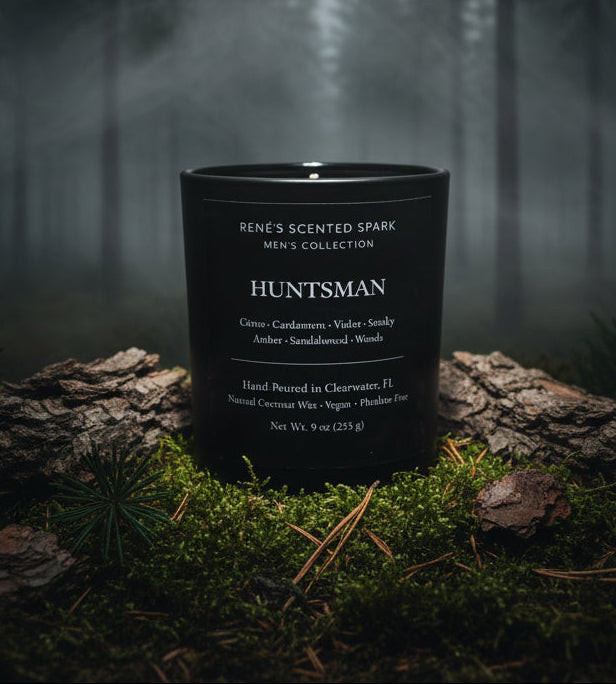 Black candle labeled 'Huntsman' from Rene's Scented Spark Men's Collection on a forest floor.