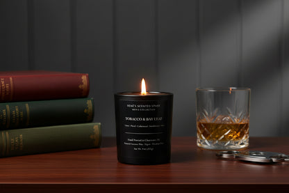Tobacco and Bay Leaf men’s scented candle burning on a wooden table beside stacked books and a whiskey glass.