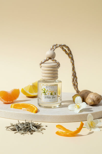 White Tea car freshener in a clear glass bottle styled with mandarin, lemon, ginger, jasmine flowers, citrus peel, and loose tea leaves on a warm cream background.