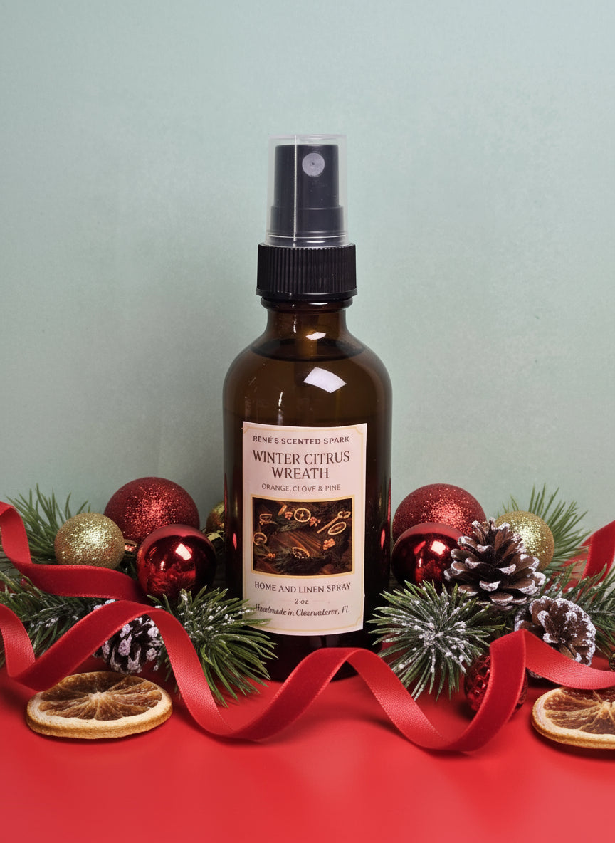 Bottle of 'Winter Citrus Wreath' room spray with Christmas decorations on a red surface.