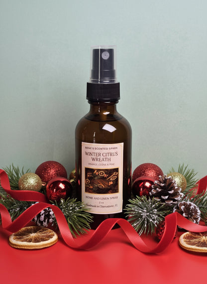 Bottle of 'Winter Citrus Wreath' room spray with Christmas decorations on a red surface.