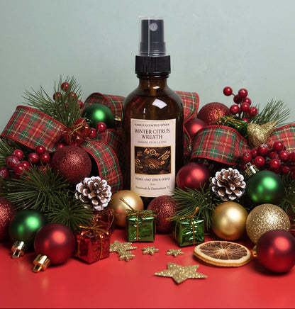 Bottle of winter citrus wreath spray surrounded by Christmas decorations on a red surface with a light green background.