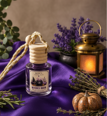 Witches Brew hanging car freshener by Renes Scented Spark styled with purple satin, a glowing lantern, herbs and a decorative pumpkin for a mystical fall setting.